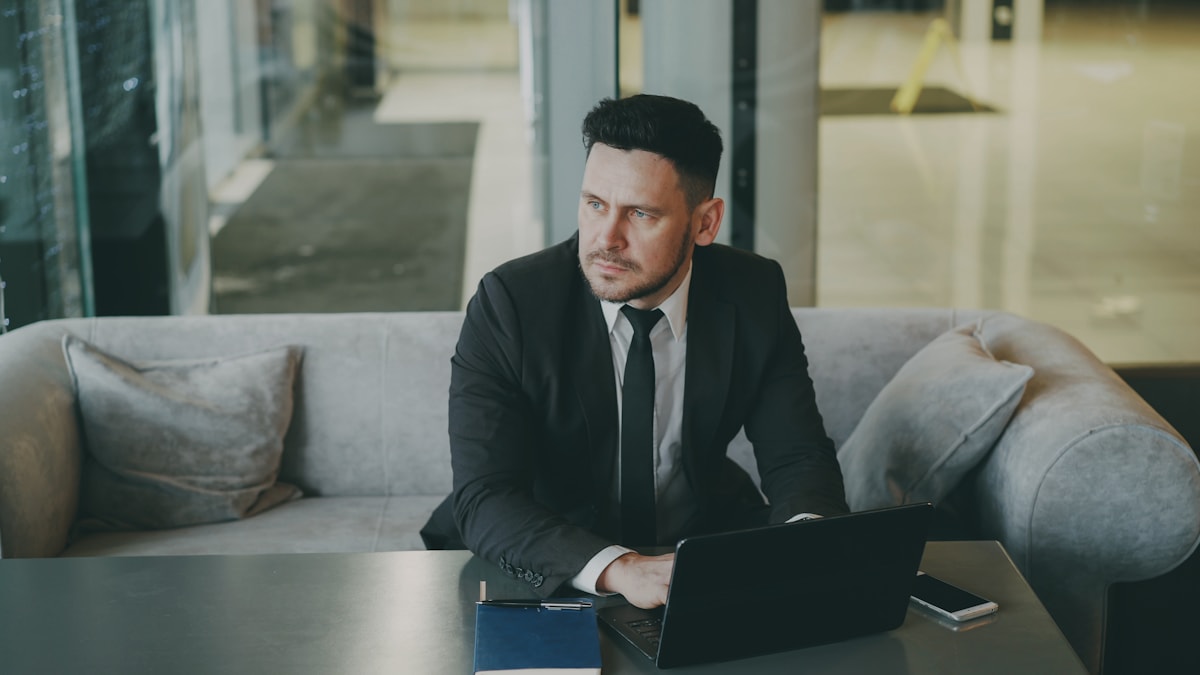 Man in suit sitting with laptop on couch.