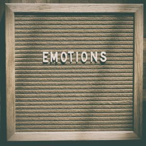 Wood-framed letter board with the word “EMOTIONS” in white letters on a textured beige background.
