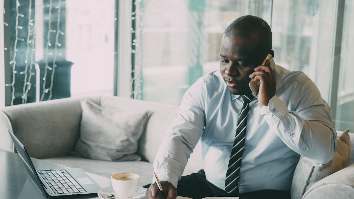 Man in shirt and tie talking on phone at desk.
