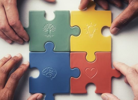 Four hands connect colorful puzzle pieces with symbols.