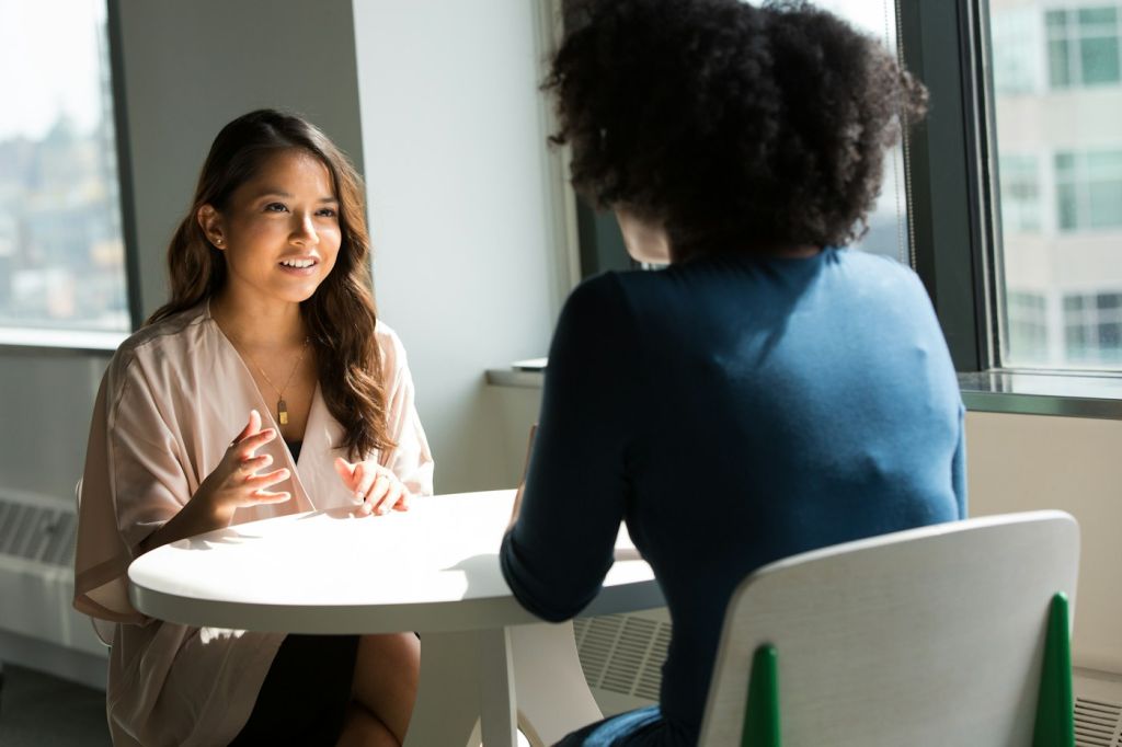 Duas profissionais conversam numa mesa de escritório, num contexto que ilustra o diálogo de reboarding.